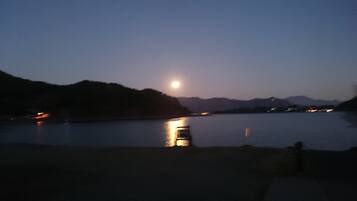 A nighttime view of a calm lake with a boat in the foreground and a mountain range in the background.