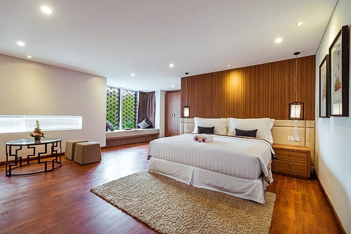 Une chambre moderne avec un grand lit, des lampes de chevet, une petite table avec un vase et une vue sur la verdure par la fenêtre.