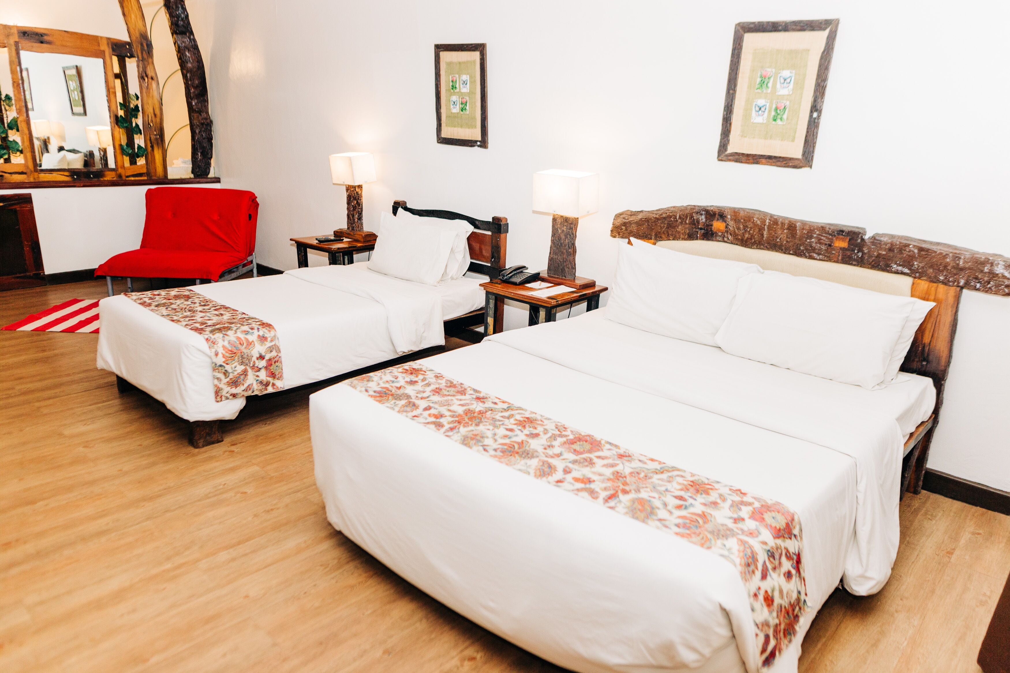 A hotel room with two beds, a red chair, and wooden flooring.