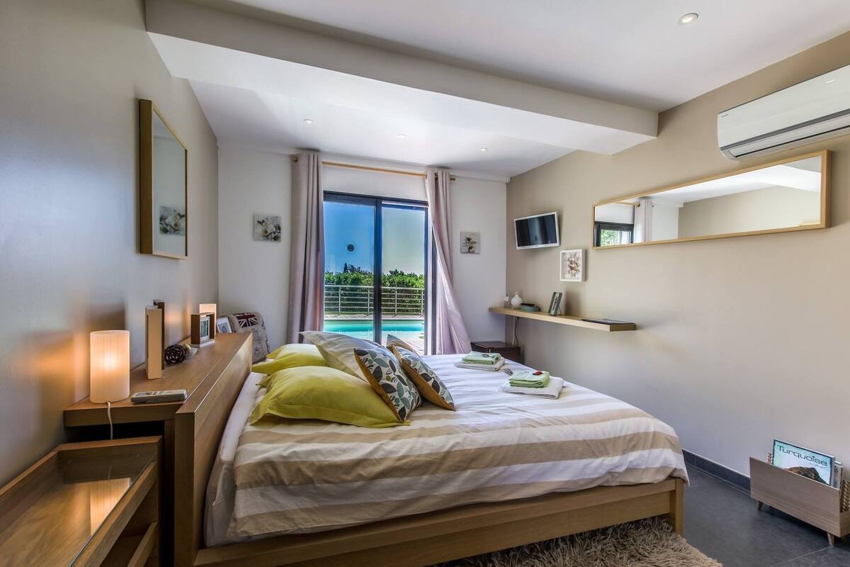 A modern bedroom with a large bed, bedside lamps, a TV, and a view of a pool.