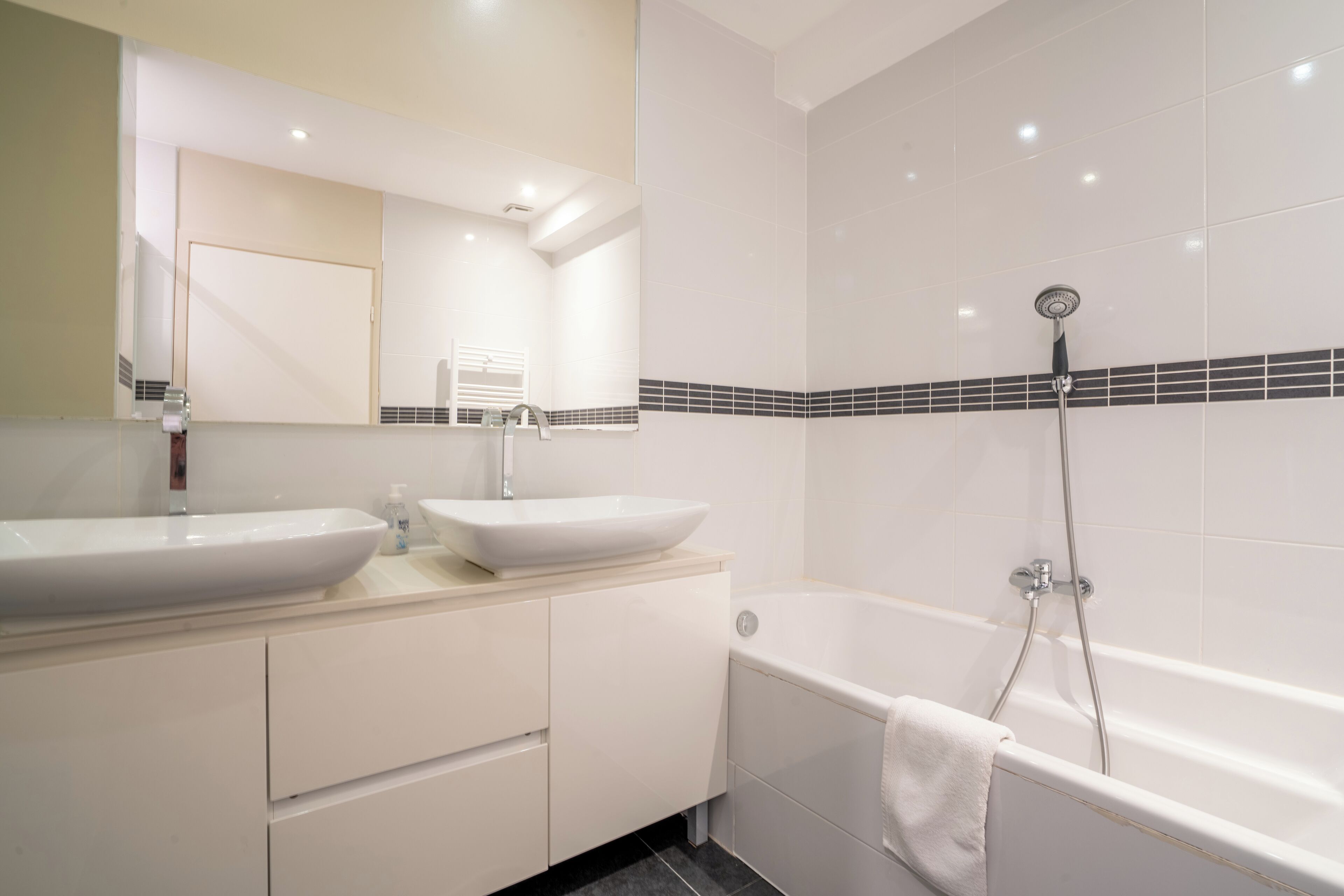 A modern bathroom with two sinks, a large mirror, and a bathtub with a showerhead.