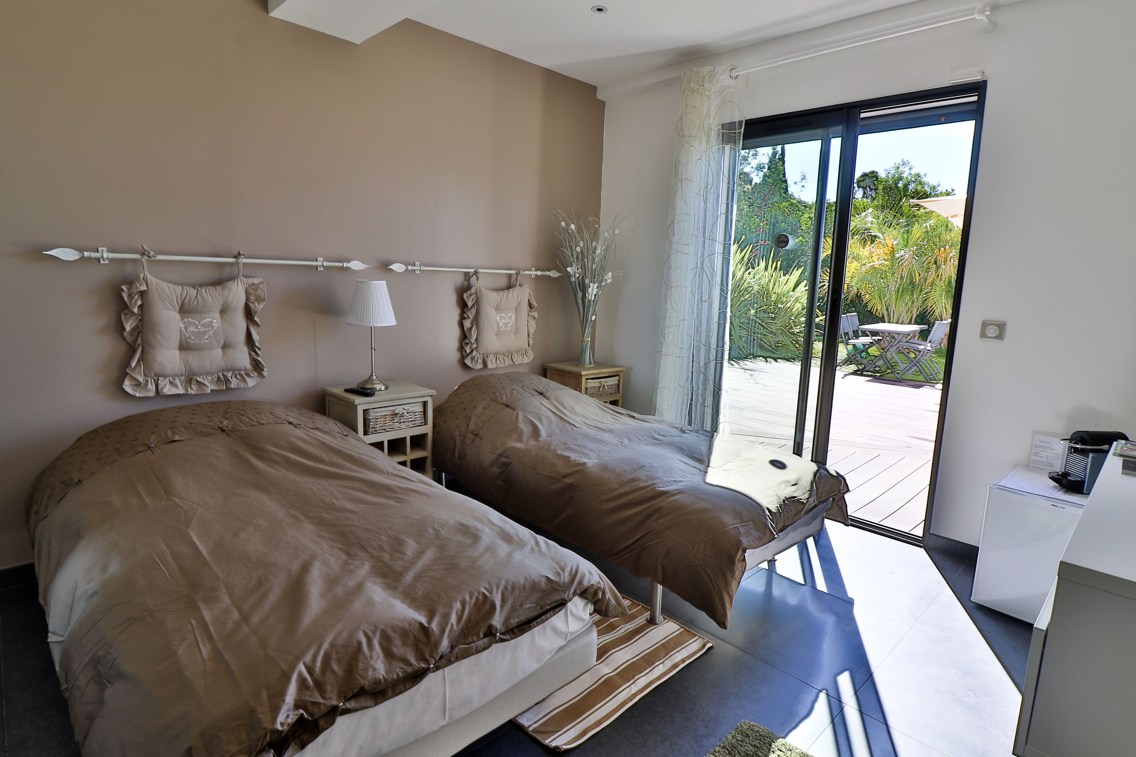 A bedroom with two beds, a nightstand, a lamp, and a view of the outdoors through a sliding door.