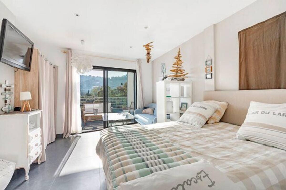 A modern bedroom with a large bed, a desk, and a view of the outdoors.