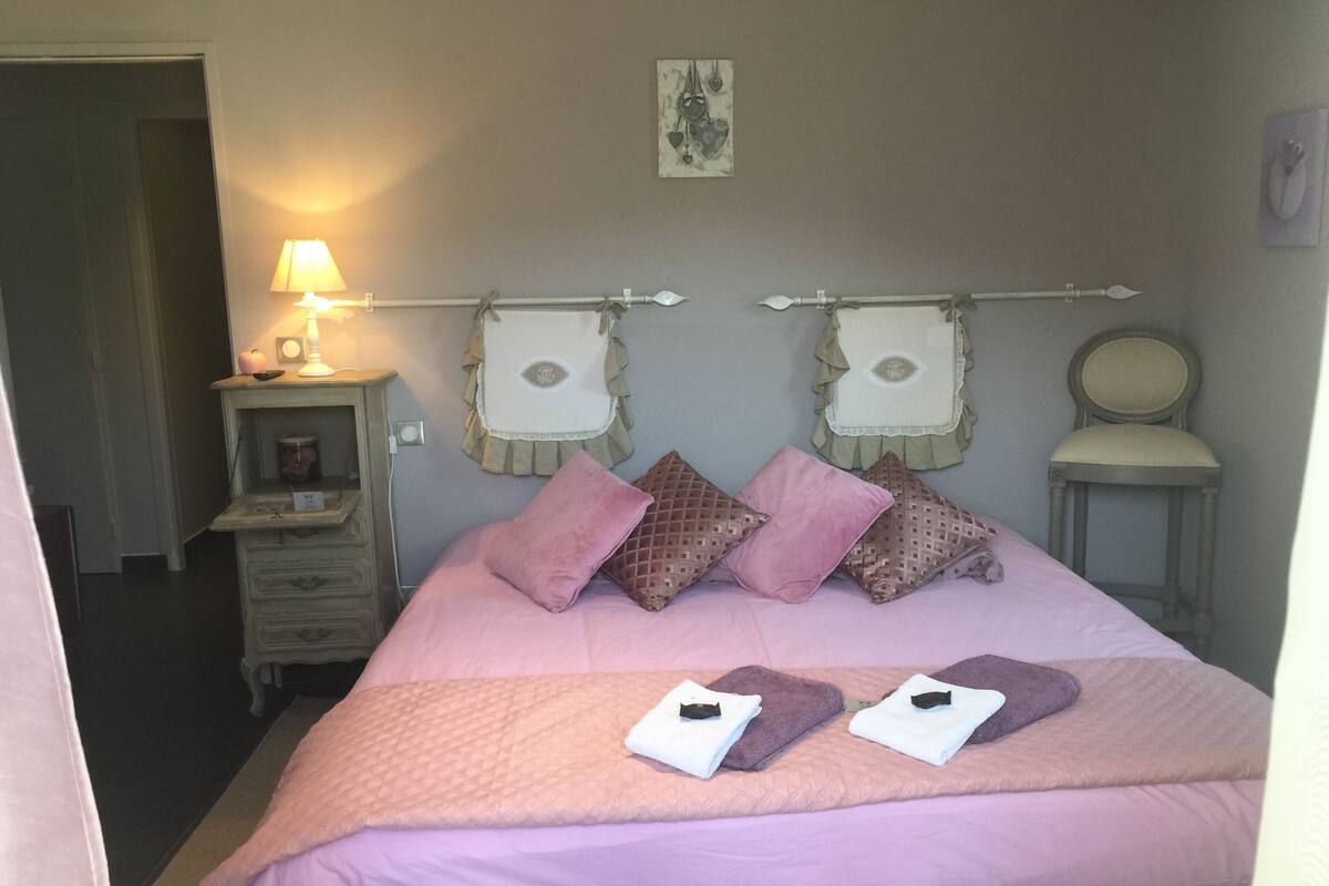 A bedroom with a bed, pillows, a nightstand, a lamp, and wall decorations.