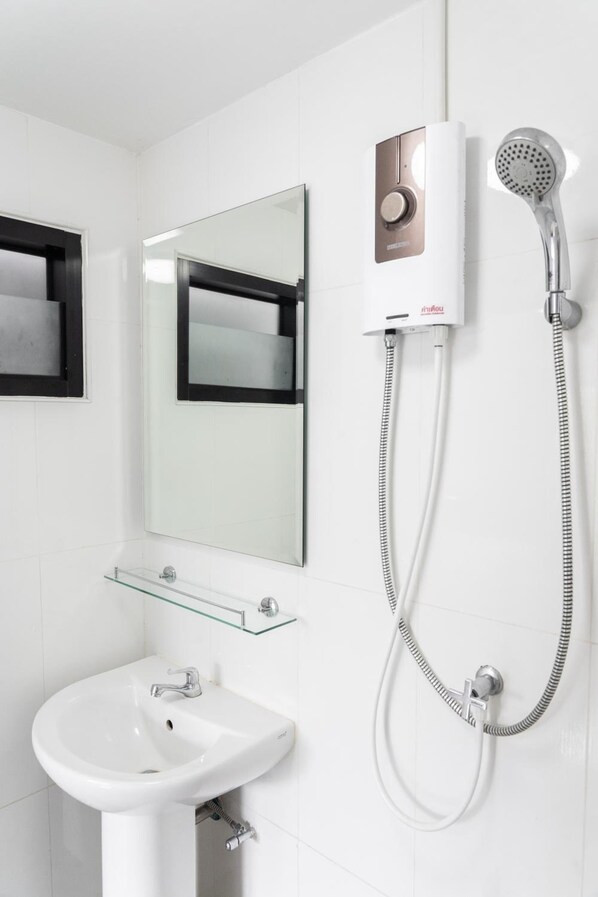 Un baño moderno con lavamanos blanco, repisa de vidrio, espejo y ducha de mano.