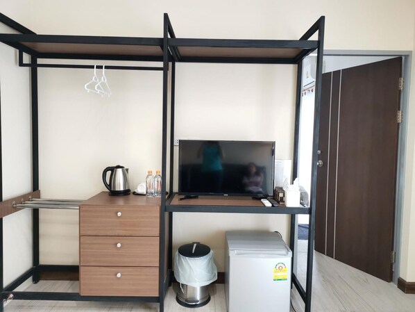A compact room with a bed, a desk, a TV, a mini-fridge, a trash bin, and a small kitchenette area. - M.I.N.D. Villa (Chiang Mai)