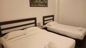 Two single beds with white linens, a small bedside table with a phone and bottled water, and a framed landscape painting on the wall.