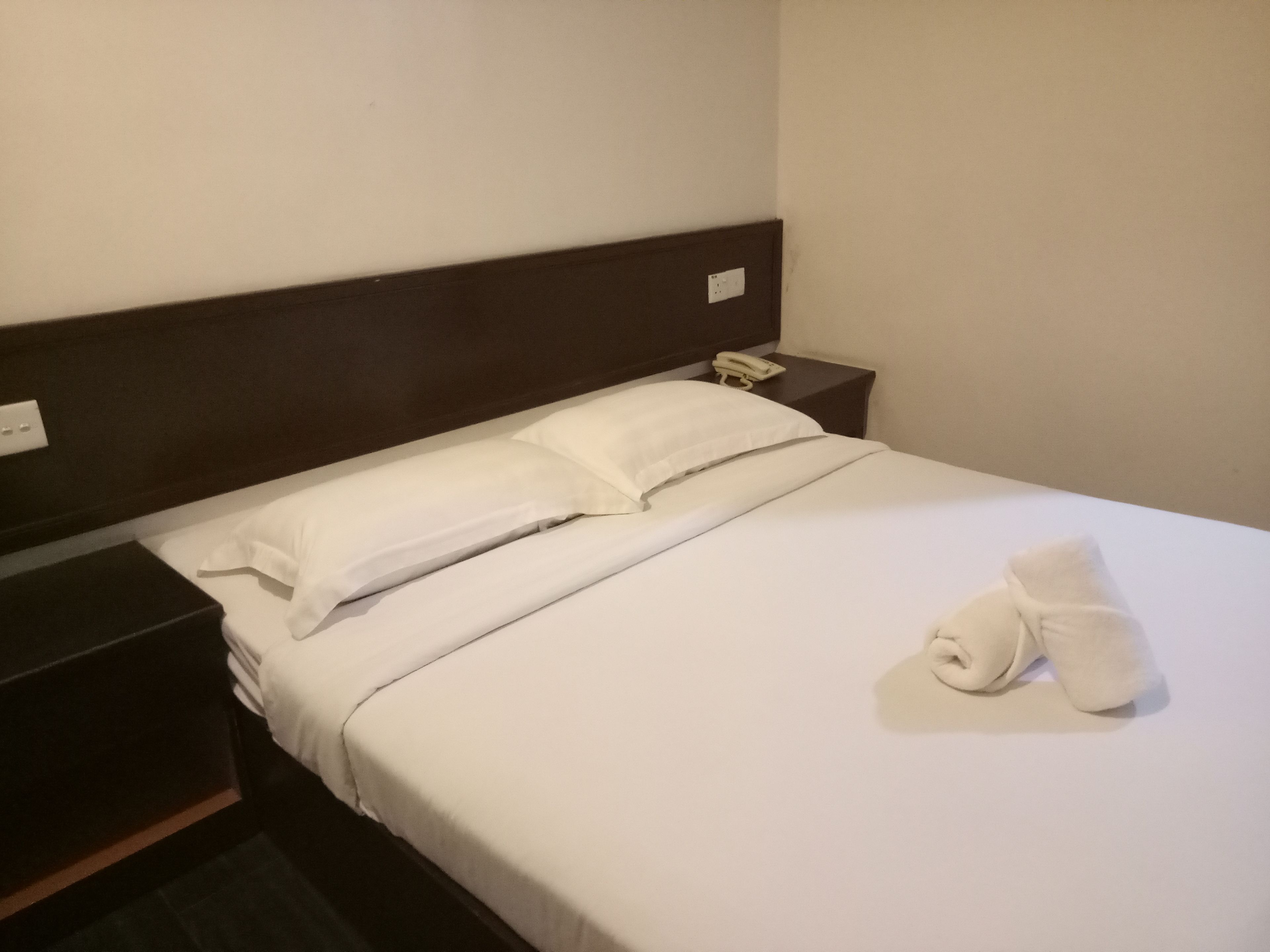 Una cama bien tendida con sábanas blancas, cabecera de madera y teléfono en la mesita de noche.