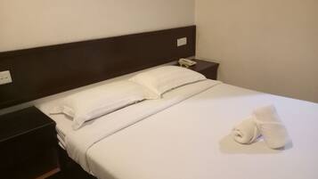 Una cama bien tendida con sábanas blancas, cabecera de madera y teléfono en la mesita de noche.