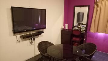 A room with a flat-screen TV mounted on the wall, a round dining table with wicker chairs, a small cabinet, and a mirror.