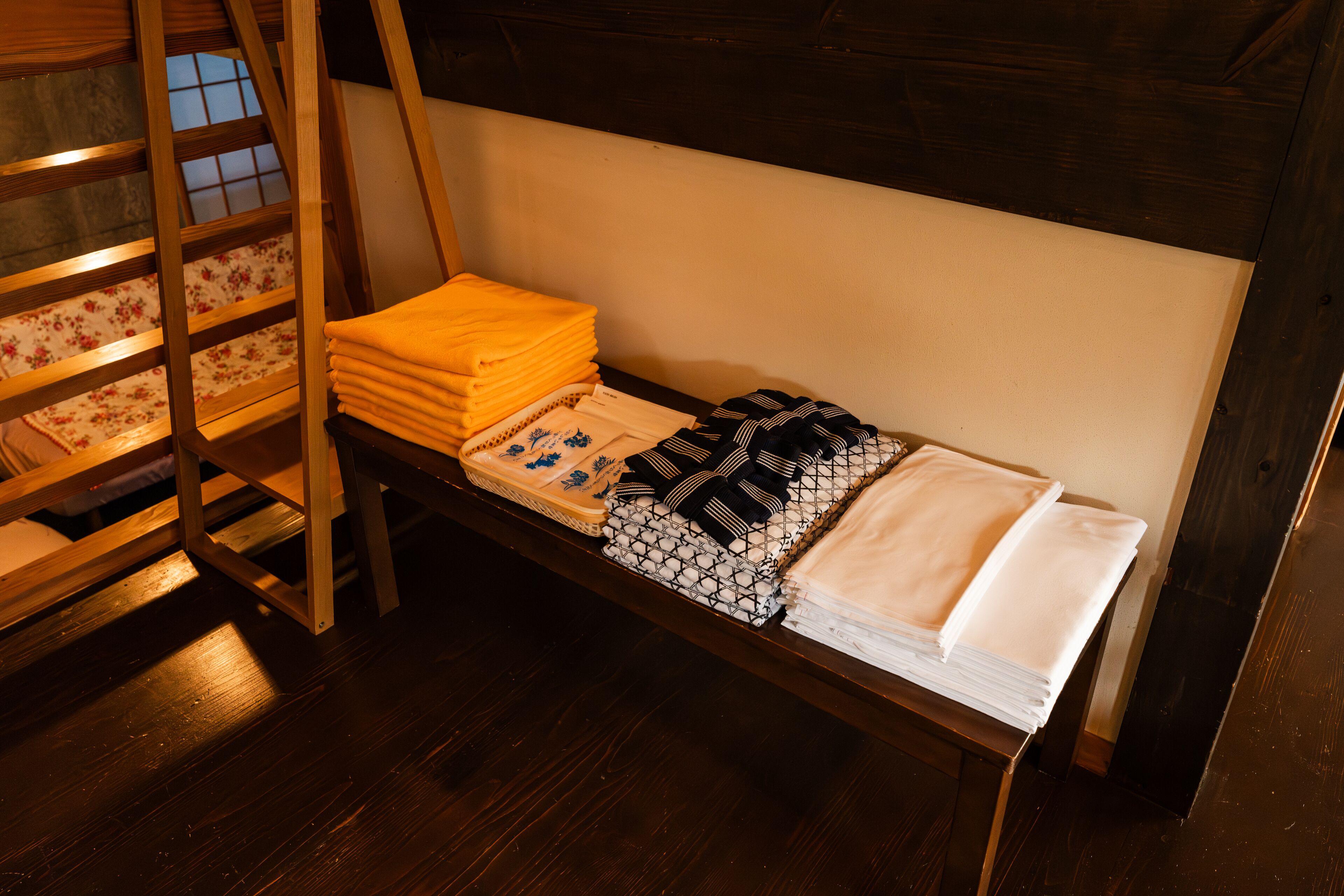 Ein Stockbett mit Holzlade, ein kleiner Tisch mit gefalteten Handtüchern und ein Fenster mit Blick ins Freie.