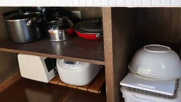 Une cuisine avec des étagères en bois où sont rangées différentes casseroles et un cuiseur à riz.