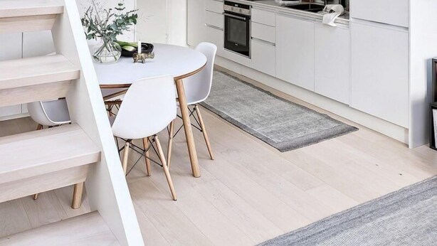 A modern kitchen with white cabinetry, a dining area with a white table and chairs, and a staircase leading to a loft bedroom.