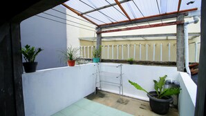 Ein kleiner, abgeschlossener Balkon mit einem Wäscheständer aus Metall, Topfpflanzen und einer weißen Wand.