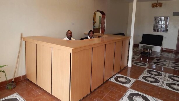 A reception desk with two individuals seated behind it, a chandelier above, and patterned floor tiles. - The Salmuc Hotel (Njoro)