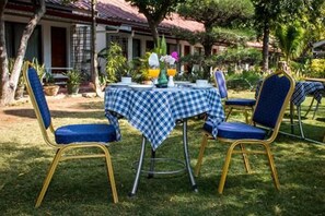 An outdoor dining area with a checkered tablecloth, blue cushioned chairs, and a tropical garden setting. - Lawkanat Hotel (Nyaung-U)