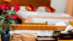 A hotel room with a bed, a vase of red roses, and a bedside table with a tissue box and a small basket.