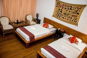 A hotel room with two beds, a wooden headboard, a small table with a vase of flowers, and a tapestry on the wall. - Lawkanat Hotel (Nyaung-U)
