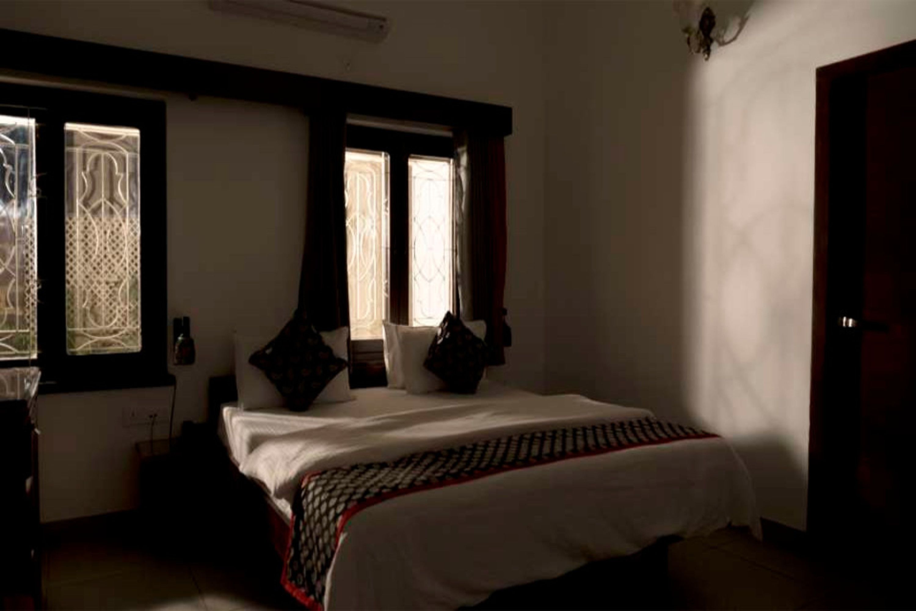A bedroom with a large bed, two windows with curtains, a bedside table, and a nightstand.