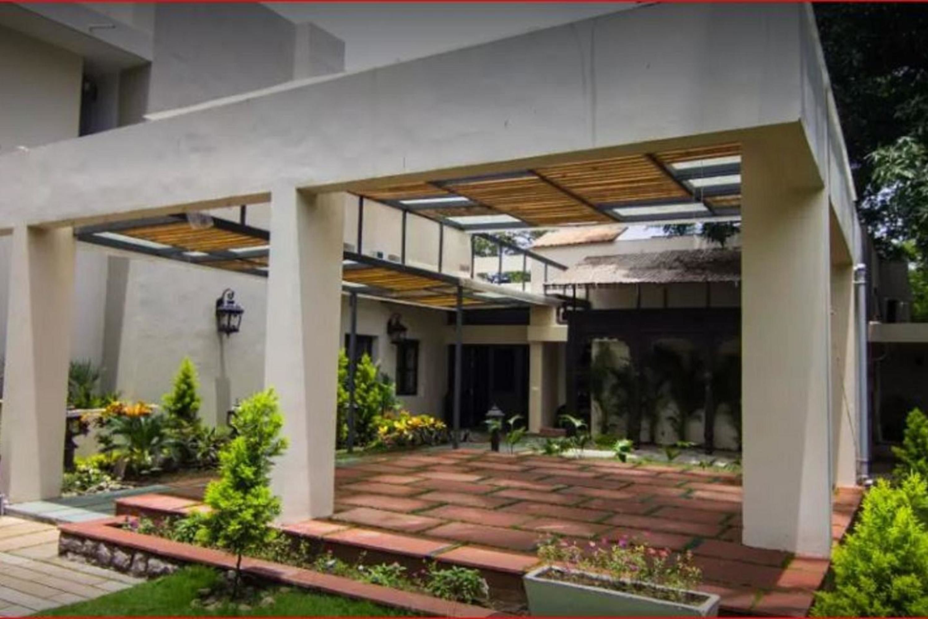 Een modern gebouw met een overdekt buitengebied, voorzien van een met bakstenen bestraat pad en plantenbakken.