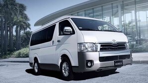 A white Hiace van parked in front of a modern building with glass windows and palm trees in the background. - Forest Inn (El Nido)