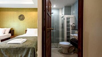 A hotel room with a bed, a bedside table, a wall decoration, and a bathroom with a toilet, sink, and shower.