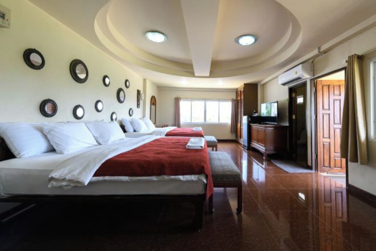 Habitación de hotel con tres camas, un televisor y una puerta de madera.