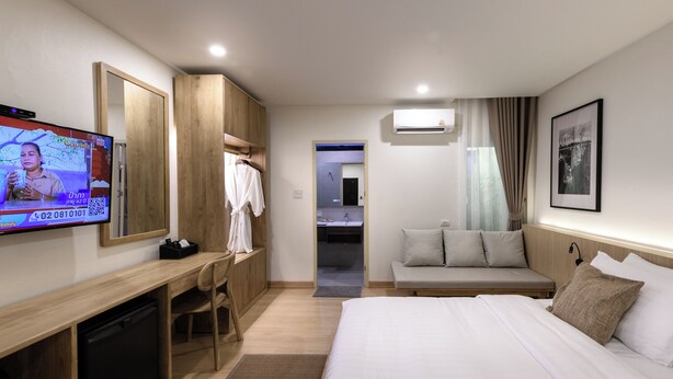 A hotel room with a bed, a desk with a TV, a wardrobe, a sofa, and an air conditioning unit. - Fahluang Residence (Phichit)