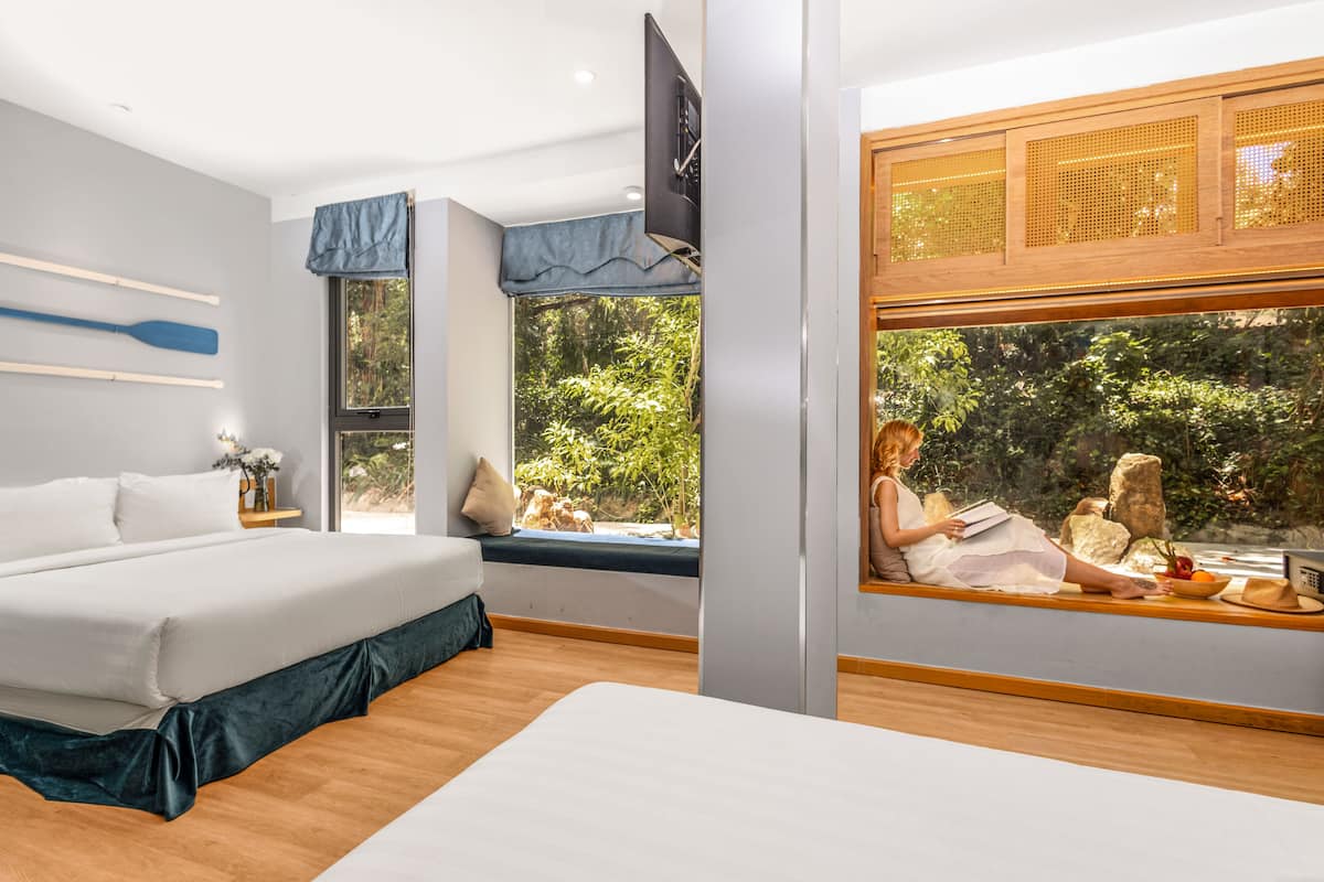 A bedroom with a large bed, a window seat, and a view of greenery.