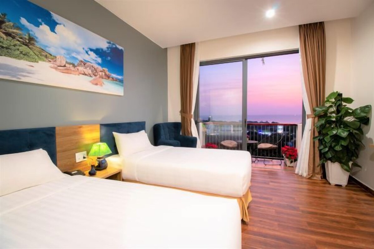 Habitación de hotel con dos camas, un ventanal con vistas, un cuadro en la pared y una planta en maceta.