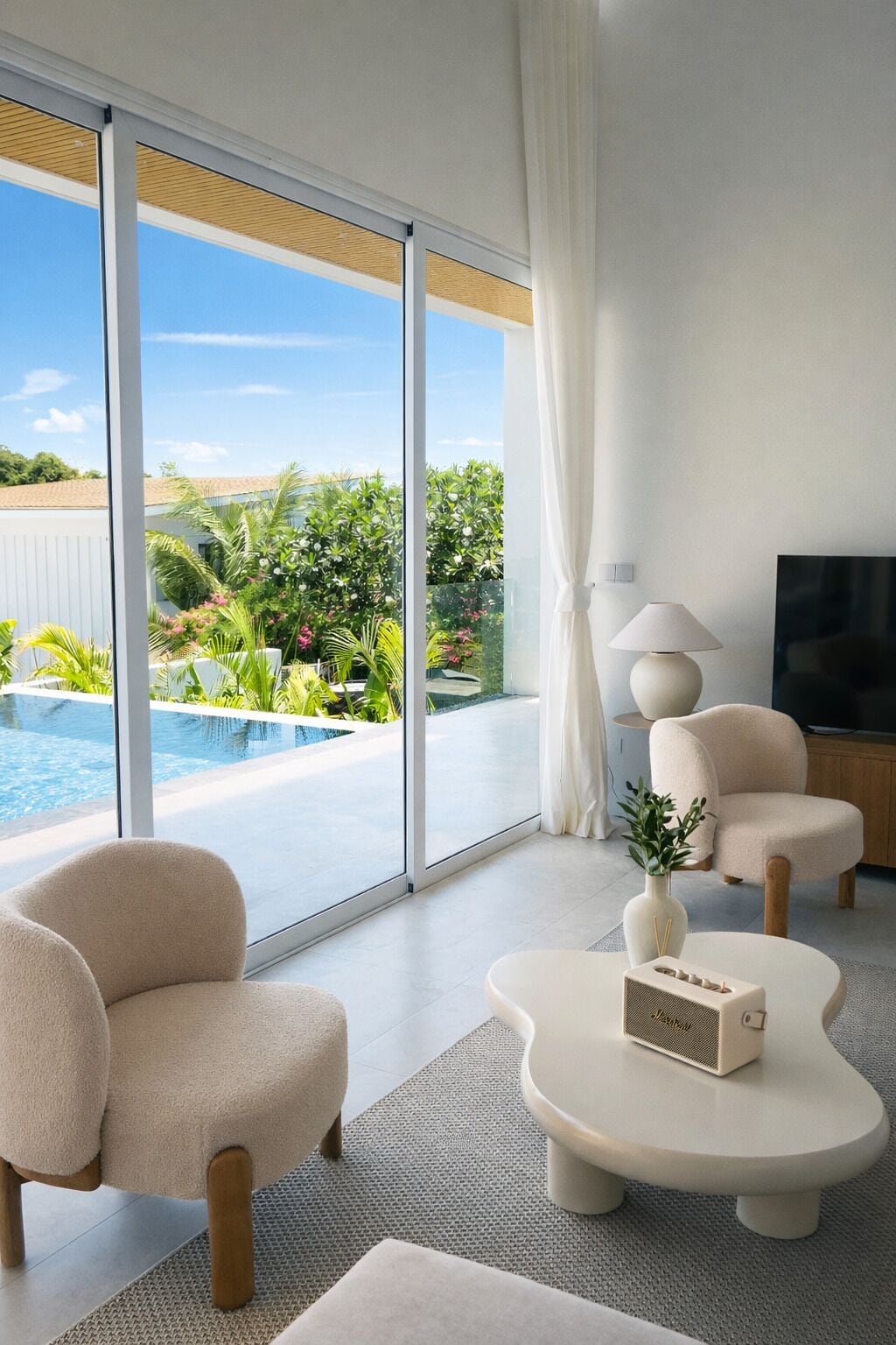 A modern living room with a large sliding glass door leading to a pool, a flat-screen TV, and a minimalist coffee table.