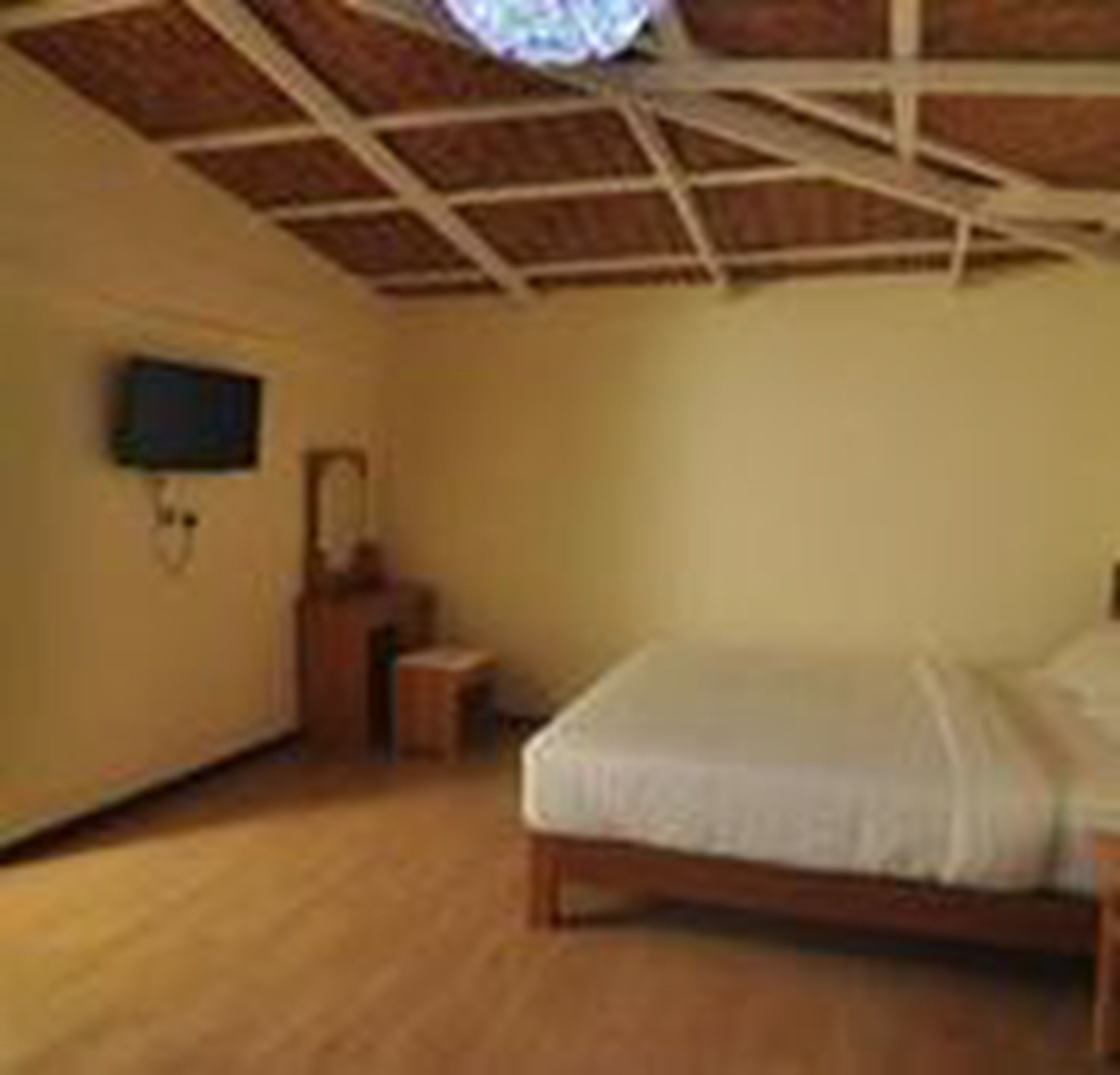 Un dormitorio con cama de madera, una mesita de noche pequeña, televisor montado en la pared y ventilador de techo.
