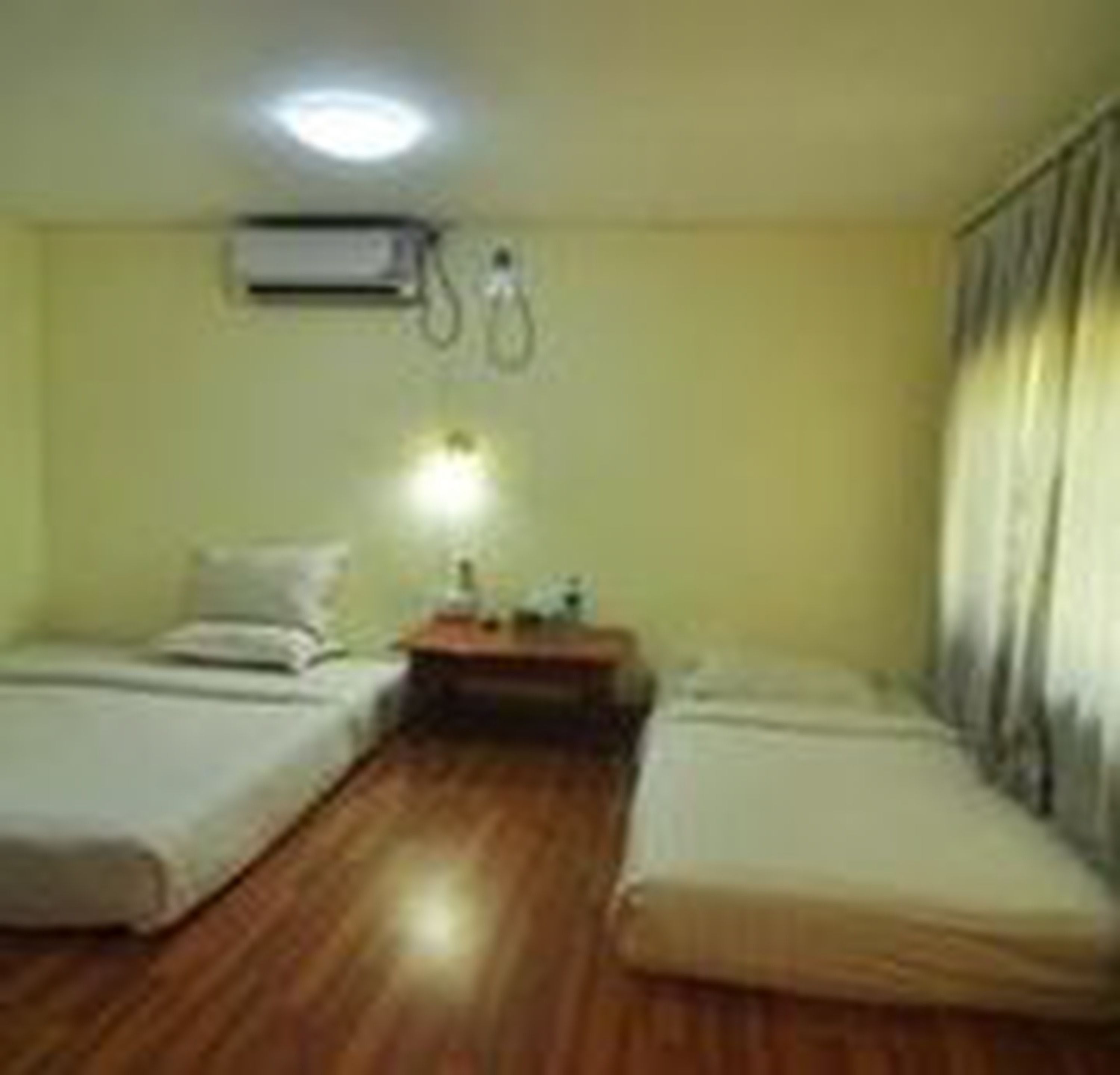 Habitación de hotel con dos camas individuales, piso de madera, mesita de noche con lámpara y un equipo de aire acondicionado en la pared.
