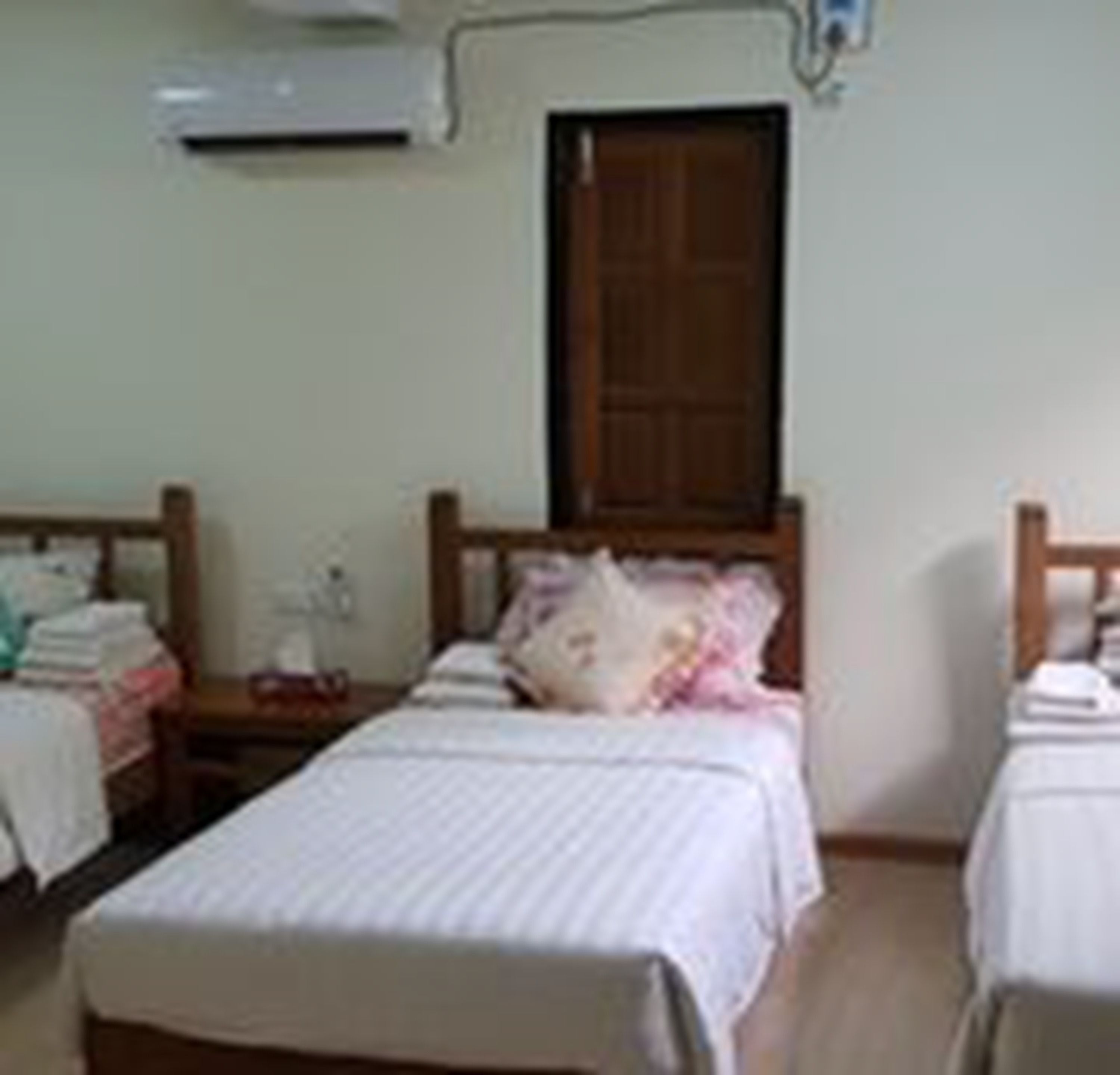 Quarto pequeno e limpo com duas camas de solteiro, porta de madeira e ar condicionado fixado na parede.