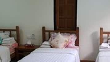 Quarto pequeno e limpo com duas camas de solteiro, porta de madeira e ar condicionado fixado na parede.
