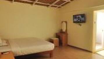 Una habitación con piso de madera, una cama, una mesita, una silla, un televisor en la pared y una puerta que da al exterior.