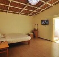 Una habitación con piso de madera, una cama, una mesita, una silla, un televisor en la pared y una puerta que da al exterior.