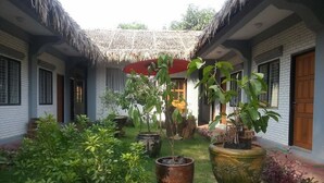 Une cour bordée de bâtiments aux toits de chaume, agrémentée de plantes en pot et d’un jardin bien entretenu.