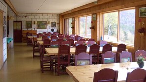 A dining area with wooden tables and chairs, large windows with views of trees, and artwork on the walls. - Voss fjellstove Rongastovo (Voss)