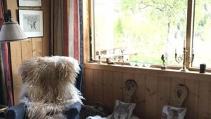 A cozy room with a blue armchair, a patterned rug, a window with a view of trees, and a wall with framed pictures. - Voss fjellstove Rongastovo (Voss)