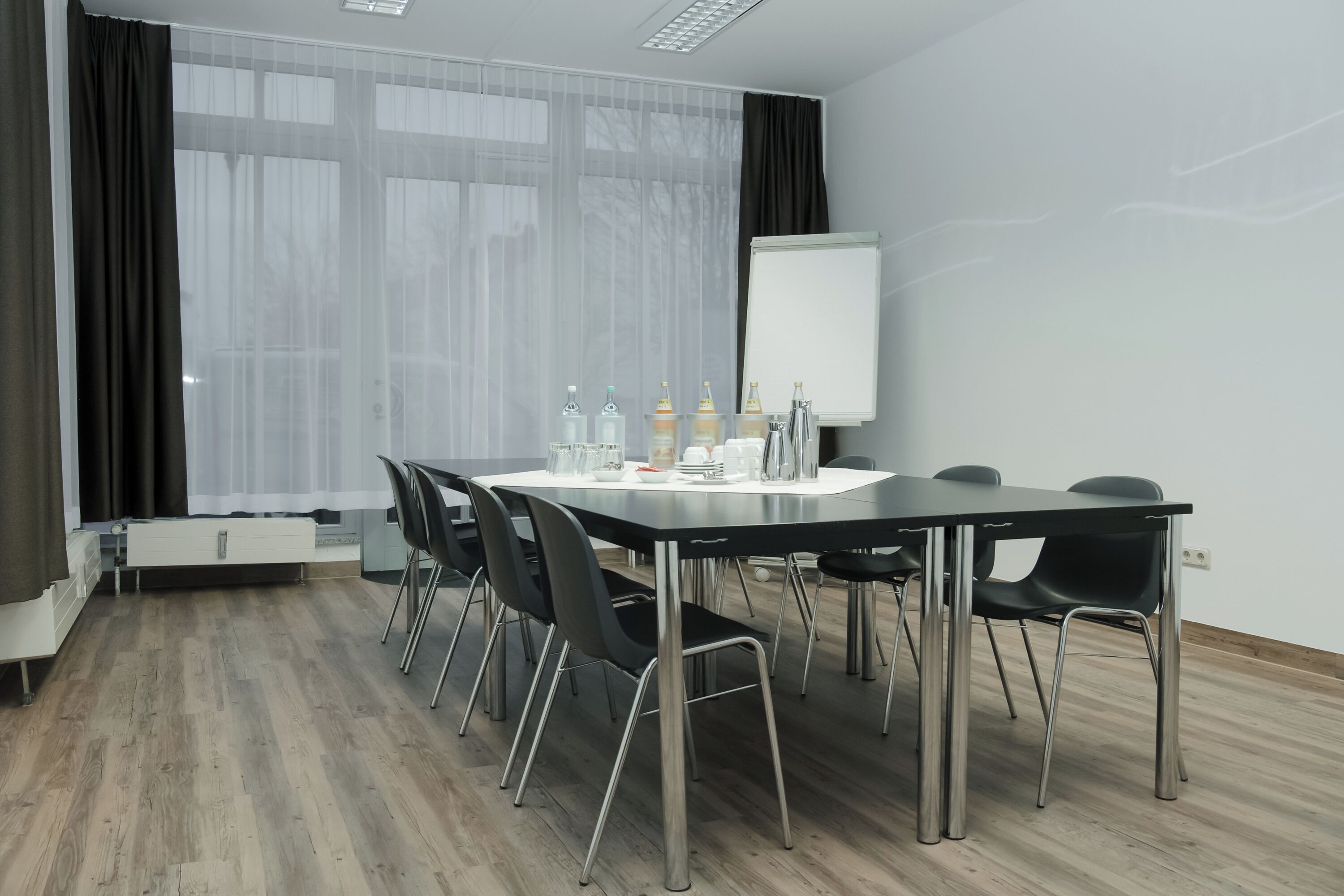 Una sala de conferències amb una taula llarga, cadires negres, una pissarra i una finestra amb cortines translúcides.