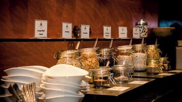 A buffet area with labeled food stations including Knusper-Mosaii Classic, Cornflakes, and Oatmeal.