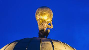 A golden statue of a figure holding a globe, set atop a dome against a blue sky.