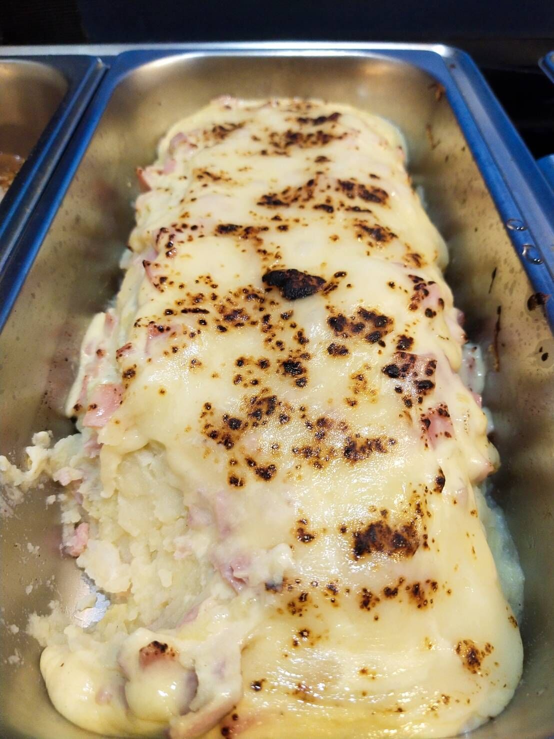 Een dienblad met een gebakken gerecht bedekt met kaas en mogelijk ham, met wat aangebakken plekjes erboven.
