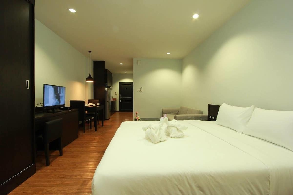A hotel room with a bed, a desk with a TV, a sofa, and a dining area.