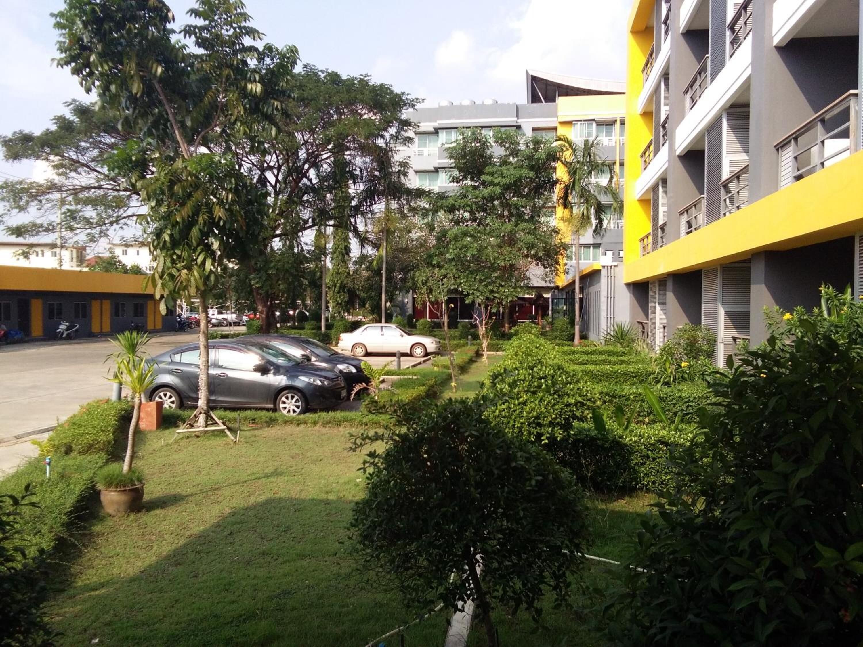 Un edificio moderno con fachada amarilla, rodeado de vegetación cuidada y automóviles estacionados.