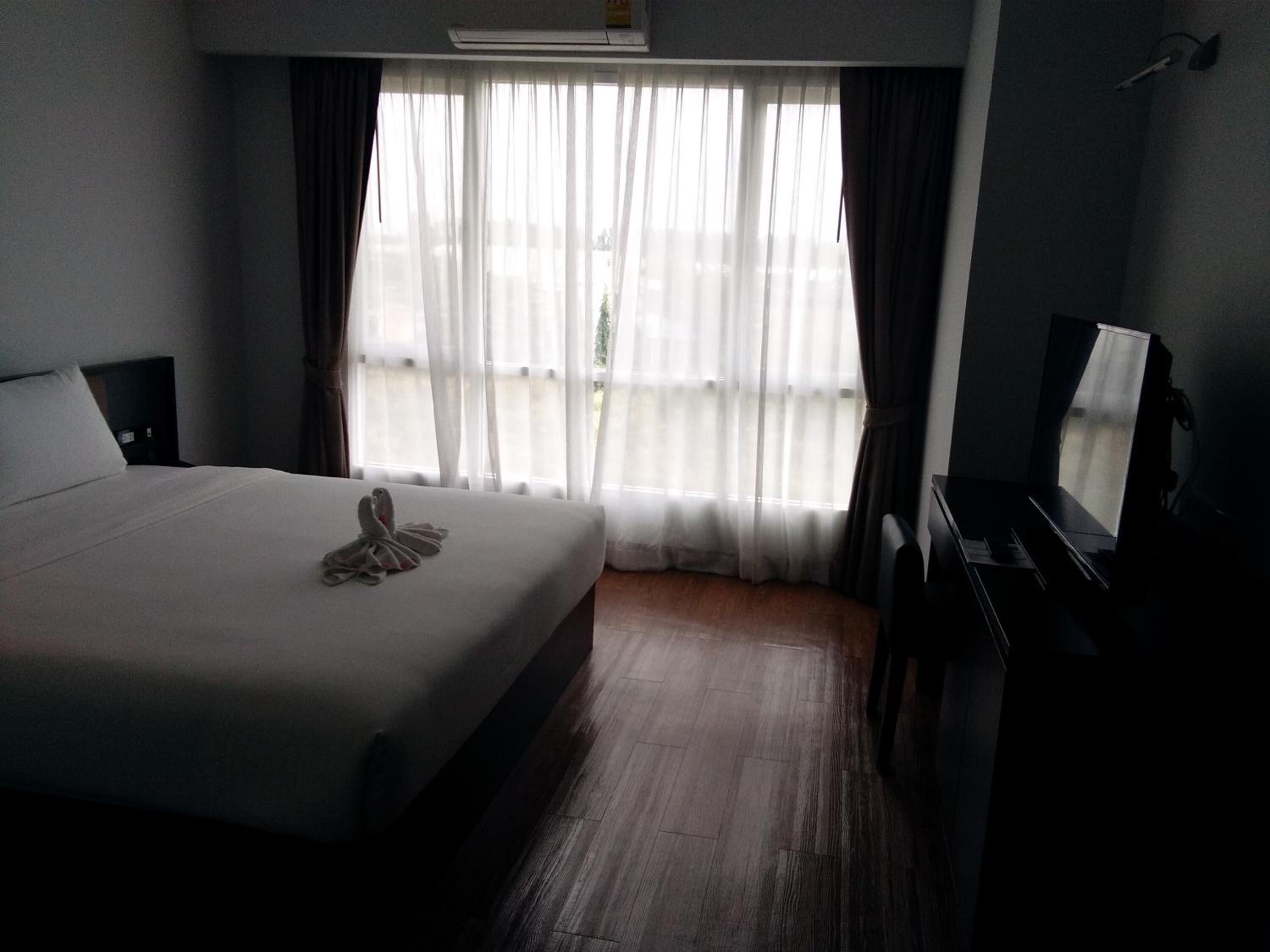 A hotel room with a bed, a desk, a chair, a television, and a window with curtains.
