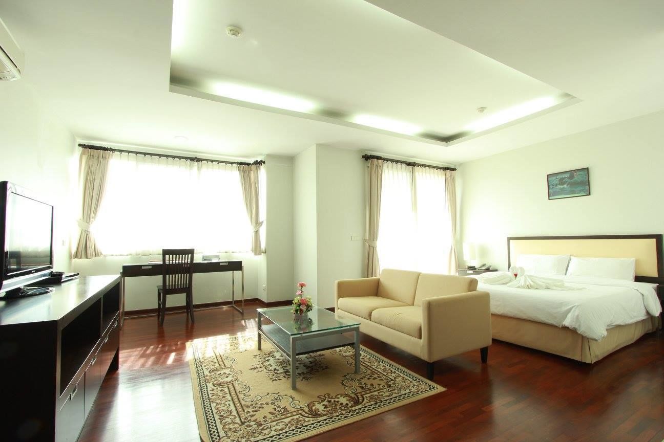 Quarto de hotel com cama, sofá, escrivaninha, televisão e mesa de centro.