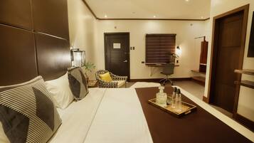 A hotel room with a bed, a chair, a desk, and a tray with bottles.