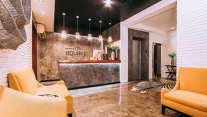 A reception area with a modern design, featuring a reception desk, a seating area with two yellow chairs, and a polished concrete floor. - The Bourke Hotel (Davao)